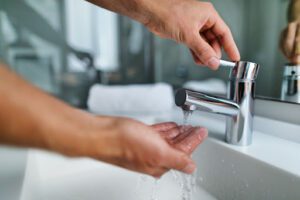 A close-up of a person's hands as they check the temperature of the water coming from a bathroom sink faucet.