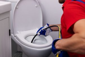 Pure Plumbing plumber insert snake into toilet to unclog it.