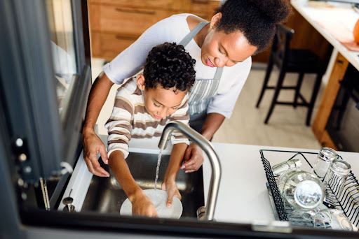 A mother and son washing a plate in a kitchen sink.