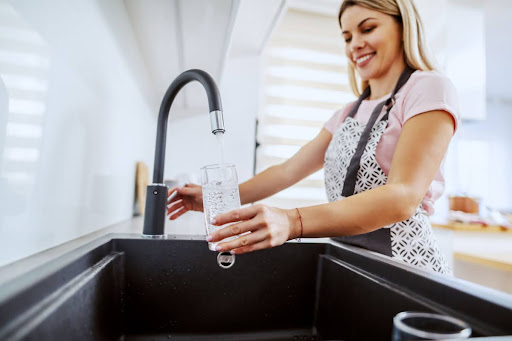 A woman filling a glass of water from a sink faucet.