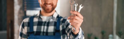 Smiling plumber holding a set of wrenches in a bathroom, ready for plumbing repair or maintenance.