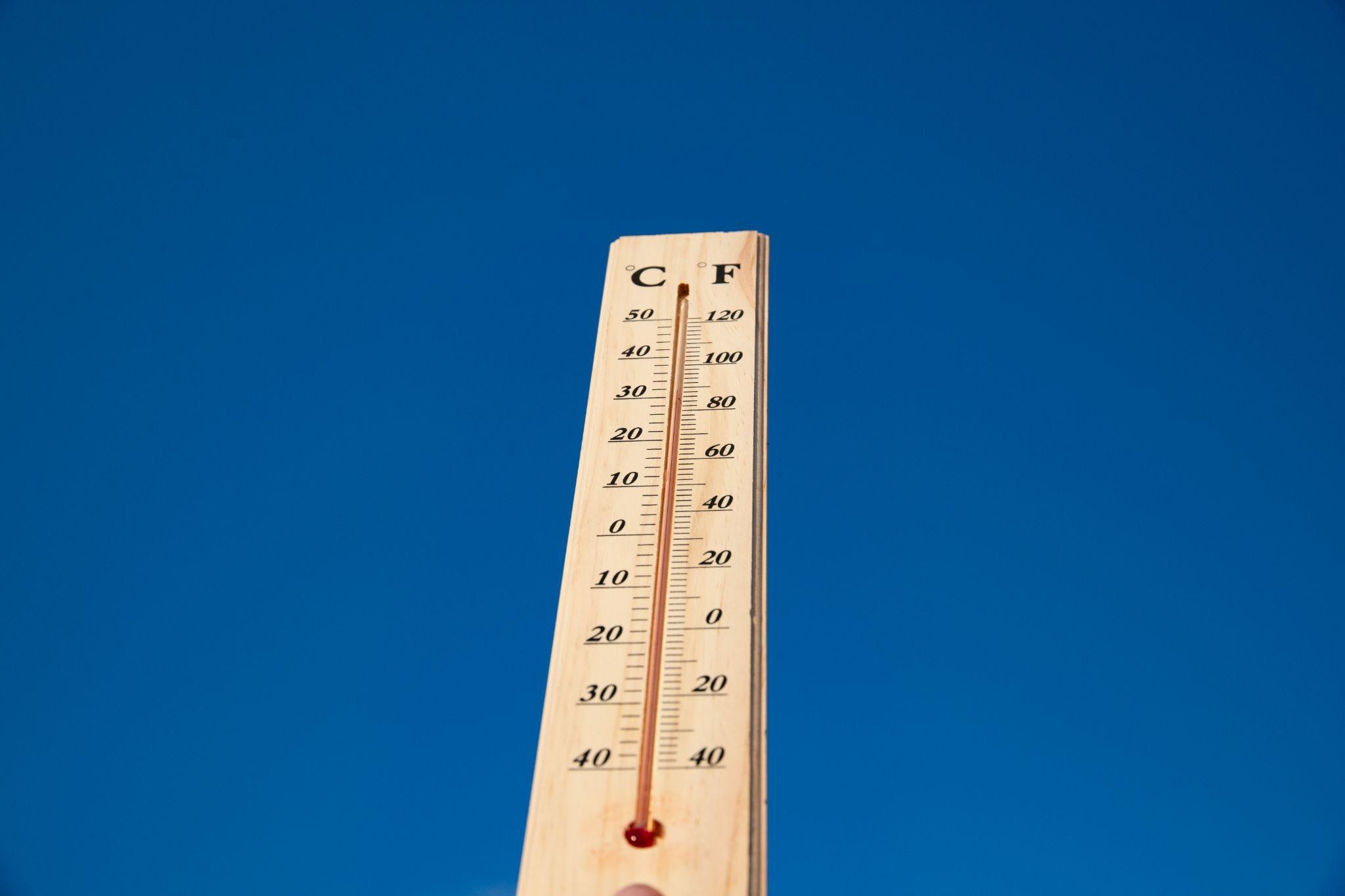 Wooden thermometer showing high temperatures under a clear blue sky, symbolizing summer heat.